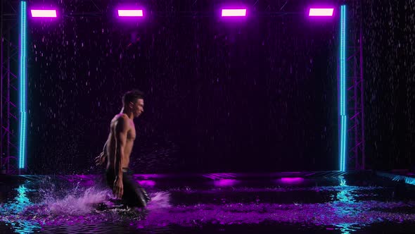 A Wet Man with a Naked Torso Slides on His Knees on the Surface of the Water in the Rain