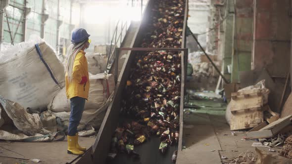 Womanworker in Yellow and Transparent Protecting Glasses Hard Hat and Mask Watching the Conveyor