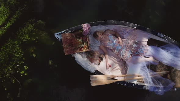 Fashion Model In Elegant Dress Lying Down On A Floating Boat - top-down drone shot