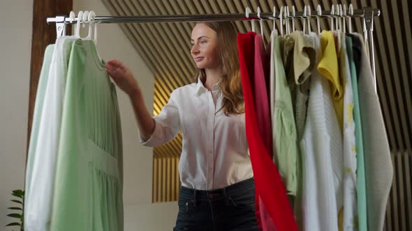 Beautiful Thoughtful Woman Stylist Chooses Clothes on a Hanger in the Dressing Room