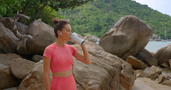 Sporty Woman in Pink Yoga Costume Rests After Yoga Exercises and Drinks Water From Bottle Outside