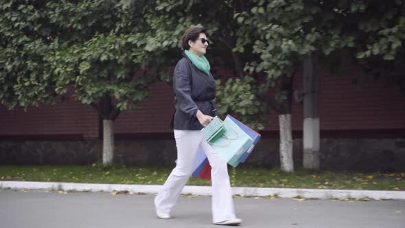 Cheerful Stylish Middleaged Woman Walking with Shopping Bags Outdoors Jumping
