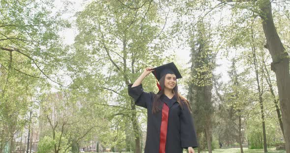 Pretty Brunette Girl Getting Off Mortarboard Jumping Throwing Up Outdoors in Park