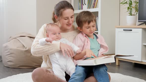 Young Loving Mother Sitting with Her Sons in Living Room and Reading Story Book