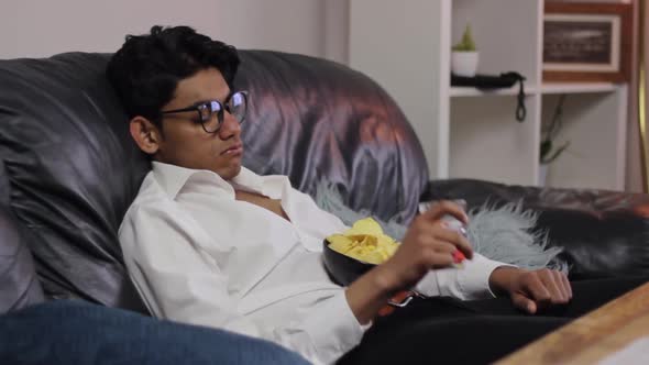 Hopeless demotivated young indian man eats junk food lying on couch, static