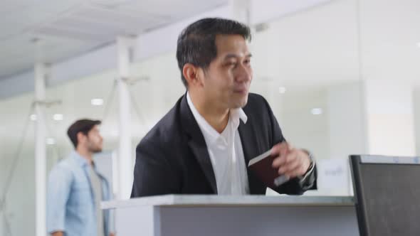 Asian businessman handing passport to airline staff at check in counter in airport terminal.