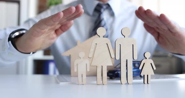 Insurance Agent Guards Figures of Family with Hands Closeup