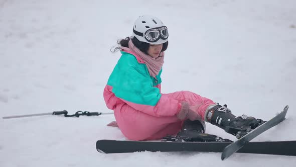 Wide Shot of Sad Young Caucasian Woman Sitting on Snow with Injured Leg