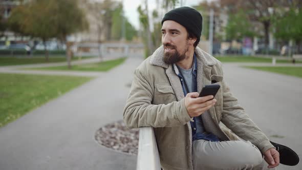 Handsome bearded man wearing hat typing by phone