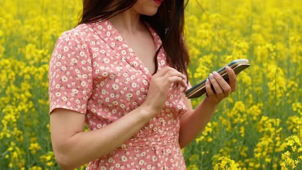 A beautiful cheerful young girl takes pictures of herself on the phone in a field