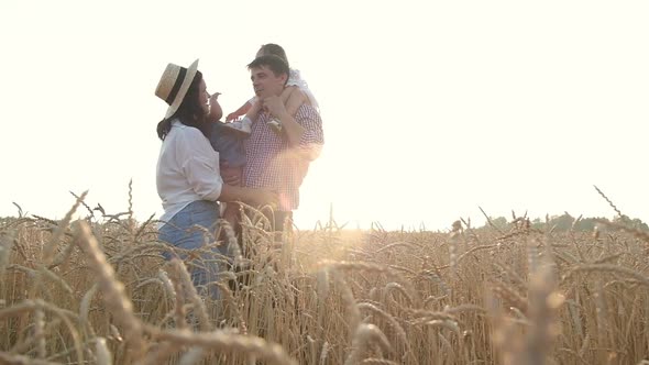 Happy mother and father with children stand in wheat field on summer day sunset