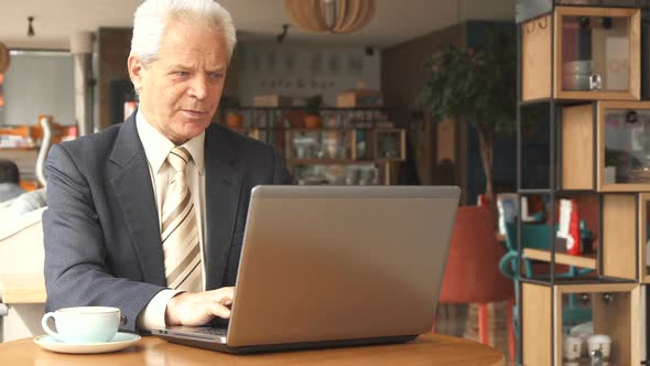 Senior Businessman Uses Laptop at the Cafe