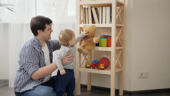 Baby boy with father taking toys from bookshelf