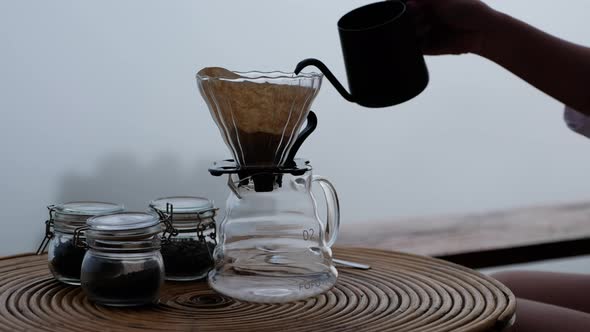 A woman pouring hot water from kettle to make drip coffee with blurred nature background