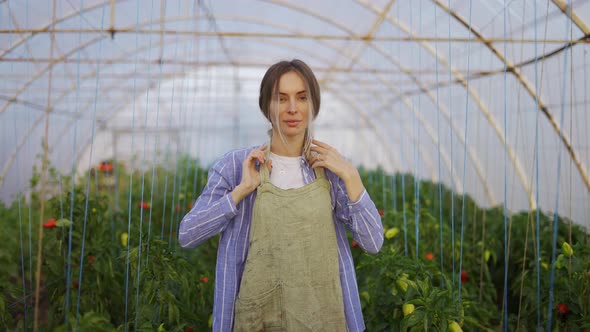 Young Woman Gardener Putting on Apron Ready for Work at Plant Shop Greenhouse