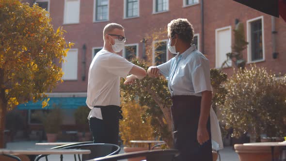 Diverse Waiters in Safety Mask Greeting Touching Elbows Standing Outdoors Cafe