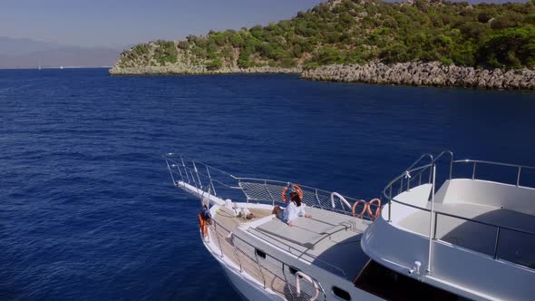 Aerial View of Floating Moored Yacht at the Rocky Coastline and Woman Sitting on It