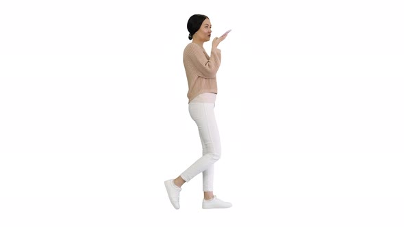 Young Woman Talking on the Phone Holding It To Her Face While Walking on White Background