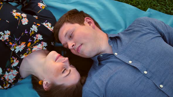 Happy Young Adult Couple Lying on the Grass Over Sunset. Smiling and Laughing