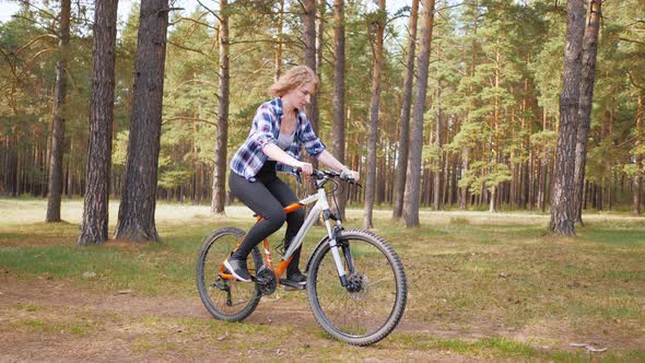 Blonde Woman Learning To Ride a Bike on a Forest Trail in Park on Green Meadow in Summer Day at