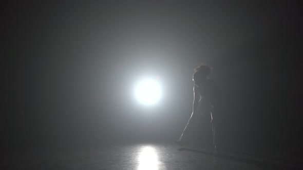 Curl Female Practicing Capoeira in Darkness Against Light Spotlight in Studio