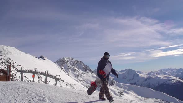 A young man snowboarder walking with his board on a scenic snow covered mountain top.