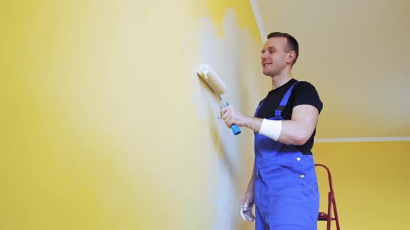 Handsome man in work overalls paints the wall with a roller