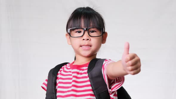 Happy schoolgirl wearing casual outfit with backpack showing thumbs up gesture on white