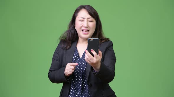 Mature Beautiful Asian Businesswoman Using Phone and Getting Bad News