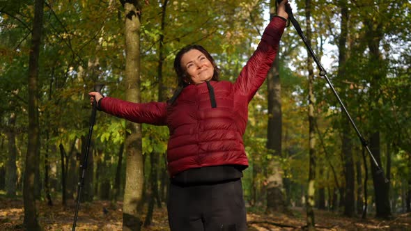 Excited Happy Mature Woman Standing in Sunshine with Stretched Hands in Autumn Park Looking Away