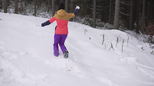 Young Happy Woman in Bright Winter Clothes Throws Snowball in the Winter Forest