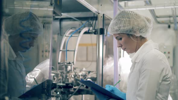 Industrial Factory Worker in Uniform Takes Notes While Factory Machine Works