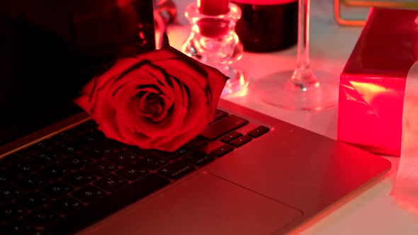 Online Date Concept Red Candles Bottle of Wine and Present Gift in Front of Laptop