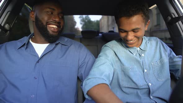 Black Teenager and Happy Father Smiling Each Other Fastening Seatbelts in Car