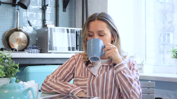 Woman drinking tea near the window. Attractive lady drinking tea at home. Cheerful woman 