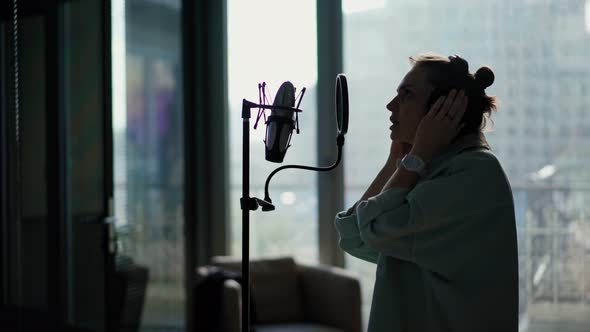 A Young Woman with Headphones Sings Into a Microphone on a Stand