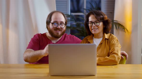 Adult Son and Aged Mother Waving Hands Having Video Call with Family on Laptop