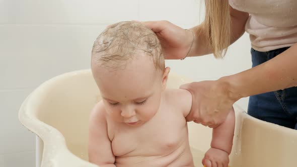 Cute Baby Boy Playing with Toy Boats While Mother Washing His Head with Shampoo