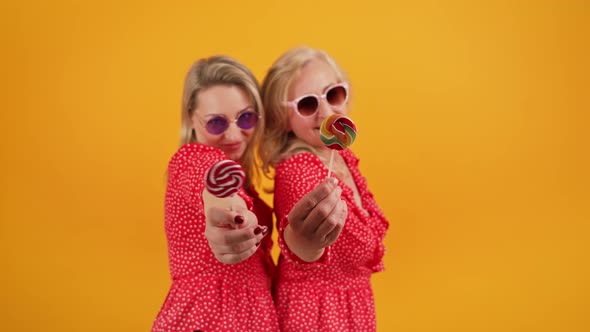 Two Blonde Excited Middleaged Women Wearing Same Red Dotted Dresses and Sunglasses Holding Colorful