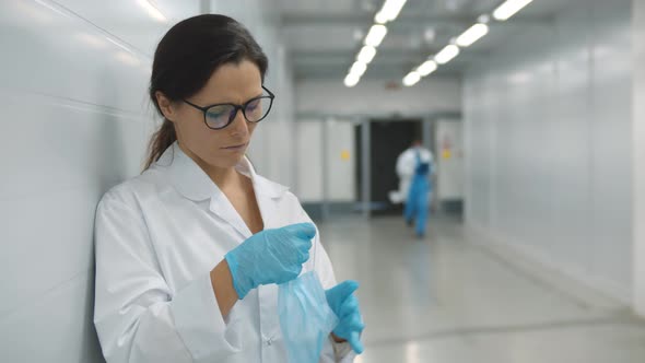 Tired Female Doctor Removing Face Mask Standing and Resting in Hospital Corridor