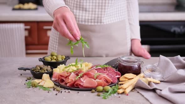 Making Meat and Cheese Antipasto Plater Woman Pouring Arugula to Serving Board with Cheese