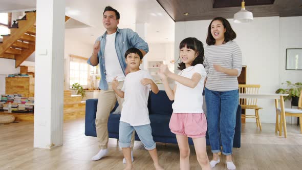 Happy cheerful Asian family having fun listen to music and dancing in living room at modern home.