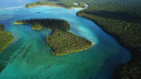 Aerial parallax around beautiful small island lit by sun in Oro Bay, Isle of Pines.