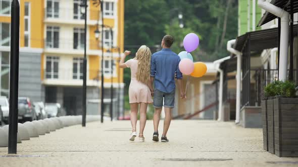 Young couple walking down street holding hands, guy holding balloons, romantic