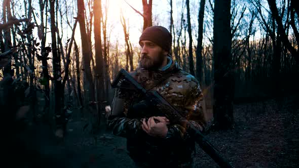 Man with a beard in camouflage with a weapon stands in the autumn forest under a leaf fall