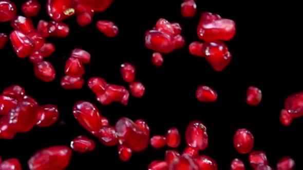 Juicy Red Grains of Ripe Pomegranate Are Flying Diagonally on a Black Background