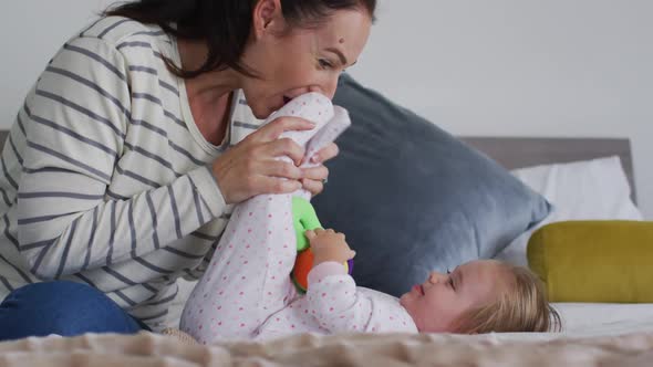 Caucasian mother playing with her baby holding a toy in the bed at home