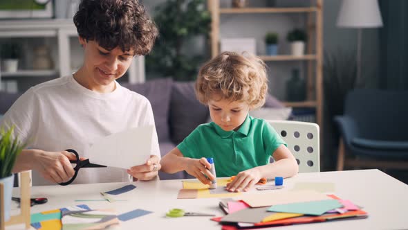 Mother and Son Doing Collages Cutting Paper and Sticking with Glue at Table