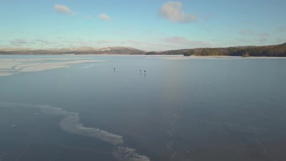 areal shot of three people ice-skating on the ice of a big lake. playfully enjoying the winter