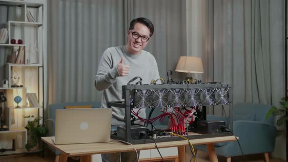 Smiling Asian Man Showing Thumbs Up While Using Laptop And Mining Rig For Mining Cryptocurrency